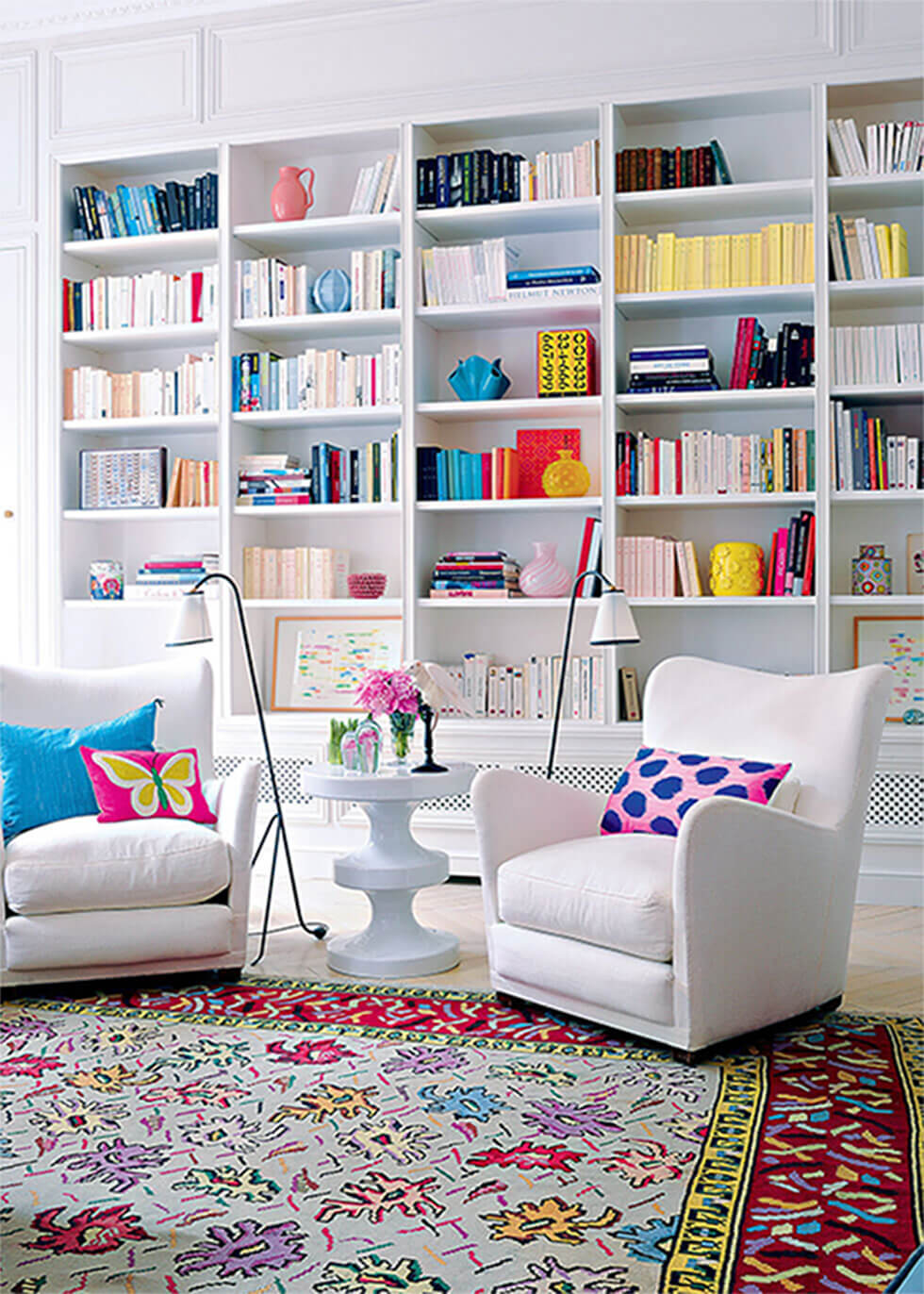 Living room with white armchairs and bookshelves, with colourful rug, cushion and decor.